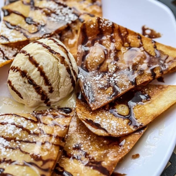 Crispy dessert nachos drizzled with chocolate and powdered sugar, served with a scoop of vanilla ice cream.