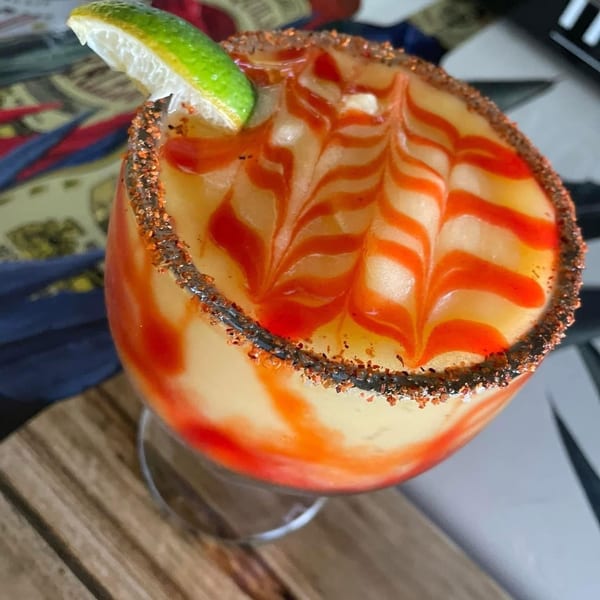 A vibrant mango margarita with red swirls, a chili-lime rim, and a lime wedge garnish.
