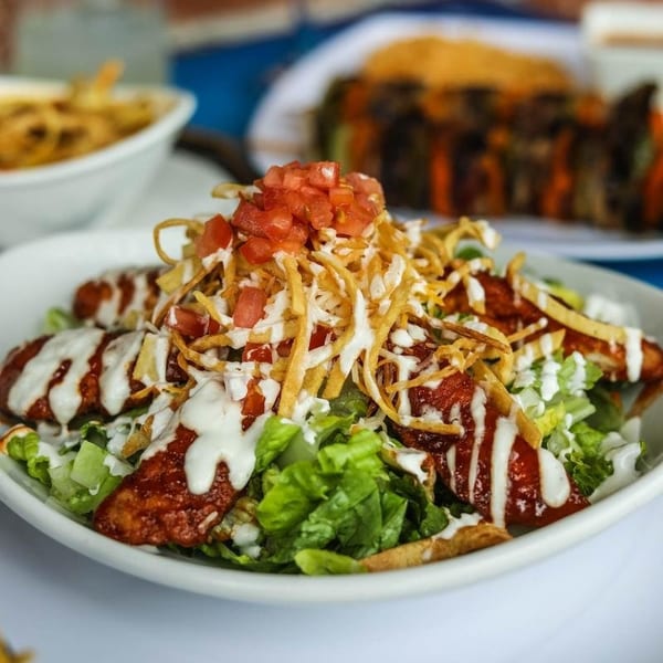 Crispy chicken salad with lettuce, tomatoes, cheese, tortilla strips, and white dressing in a bowl.