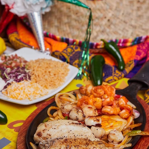 Sizzling seafood fajitas with fish, shrimp, and scallops, alongside rice, cheese, and salsa.