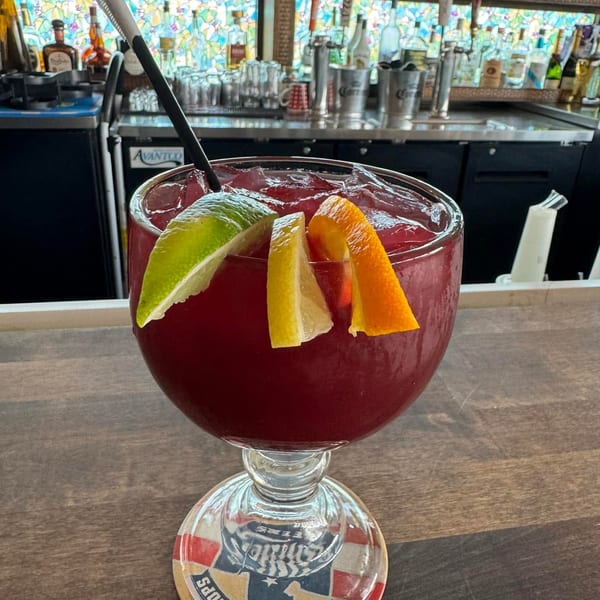 A large red sangria with lime, lemon, and orange slices on a wooden bar top.