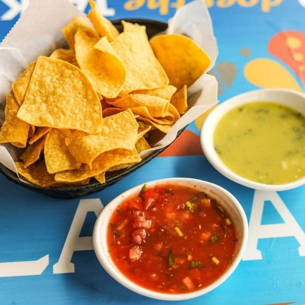 A basket of tortilla chips with bowls of red salsa and green salsa on a blue table.