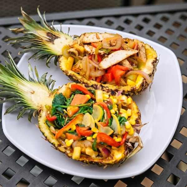 Two pineapple halves filled with colorful stir-fried vegetables and chicken on a white plate.
