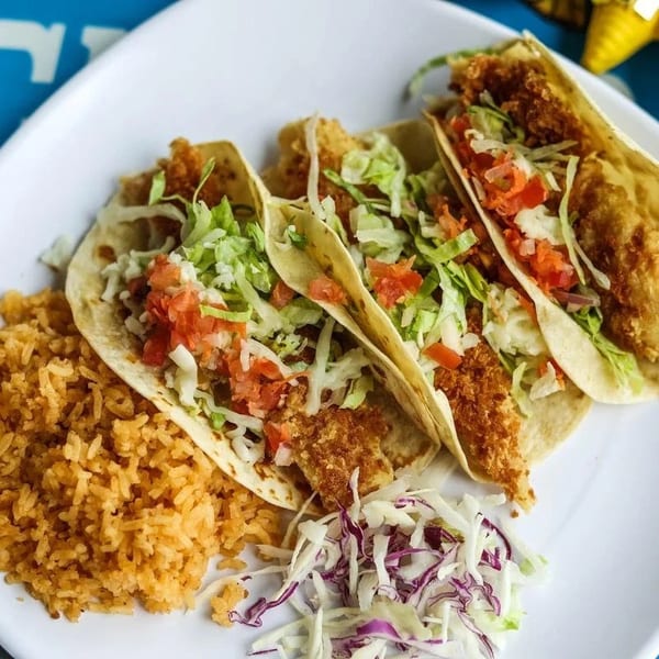 Three fish tacos with rice and coleslaw on a white plate.