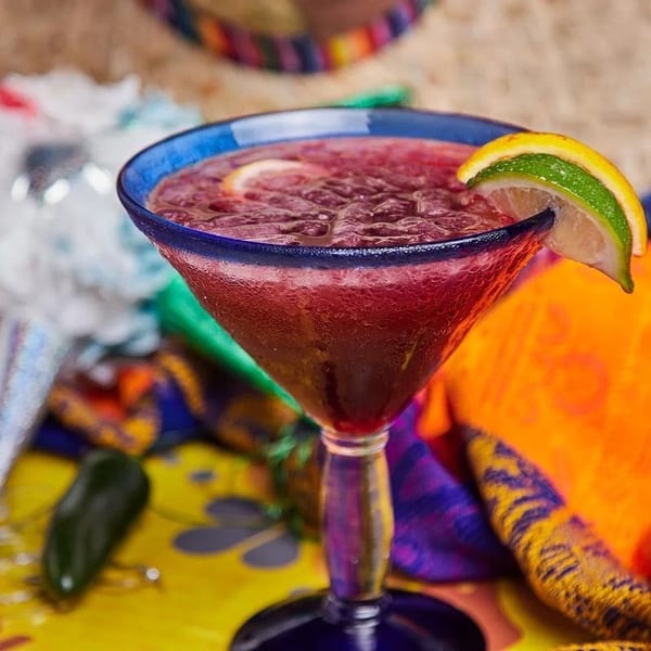 A vibrant red frozen margarita in a blue-rimmed glass, garnished with lime and lemon slices.