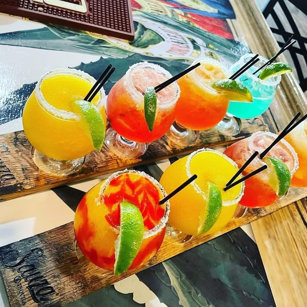 Colorful margaritas with lime wedges and straws, served on wooden Sauza Tequila branded trays.